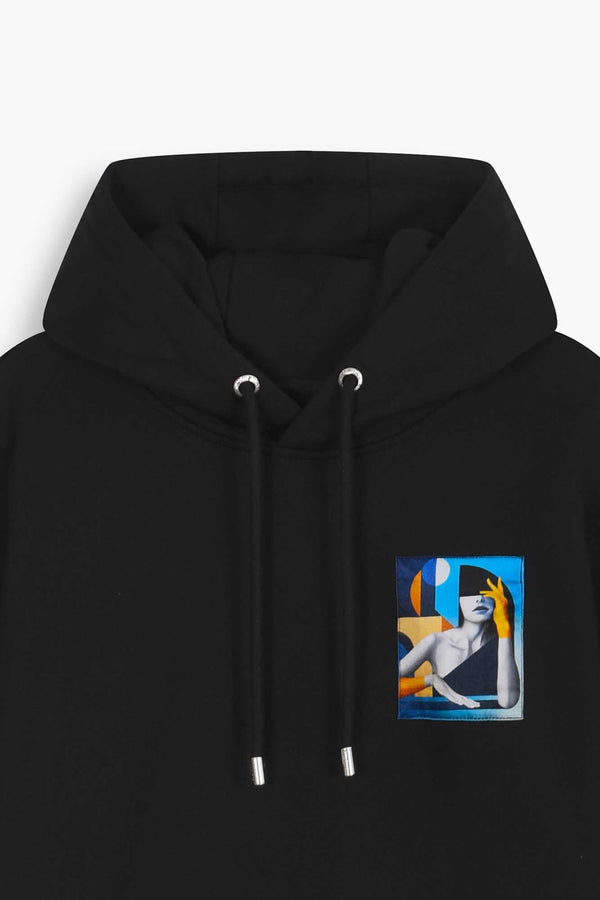 Détail Hoodie noir avec oeuvre "Riviera" en miniature sur le coeur du vêtement. Collection capsule avec l'artiste français SKIO